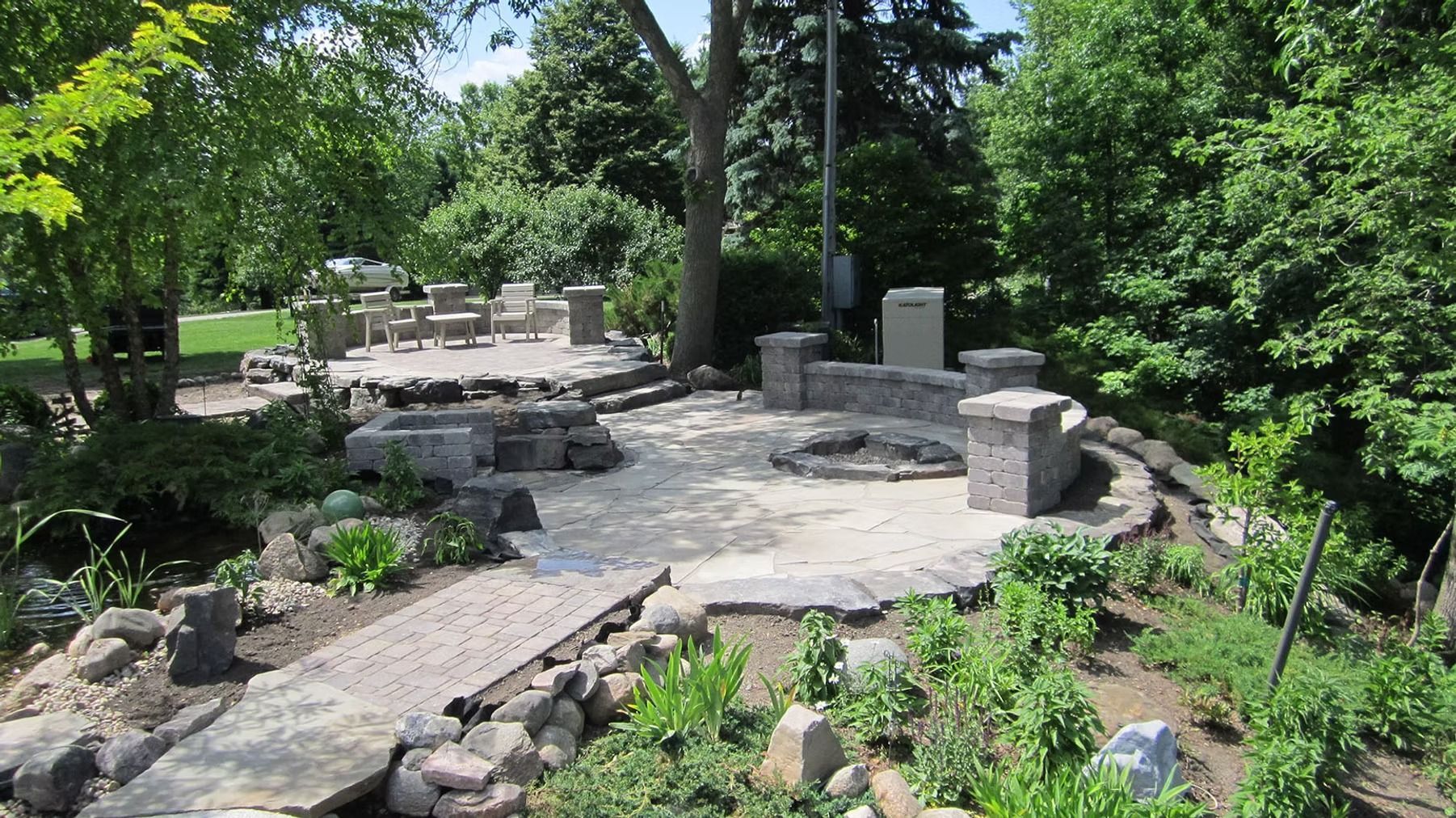 Stone patio garden with curved seating, surrounded by trees and greenery.