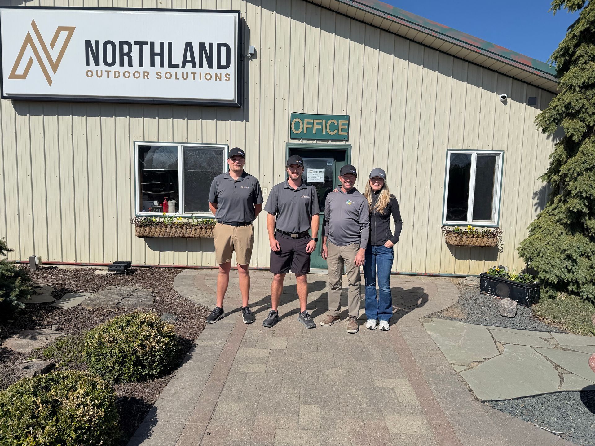 Four people standing outside Northland Motorcars office building with a sign above the door