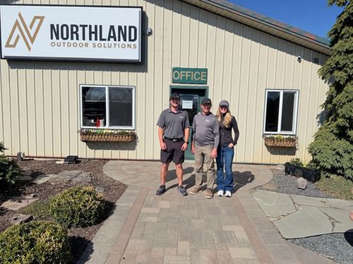 Three people stand outside the Northland Outdoor Solutions office building.