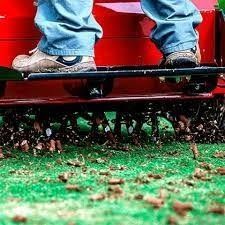 Boots and jeans on a red tractor tilling soil with dirt flying up