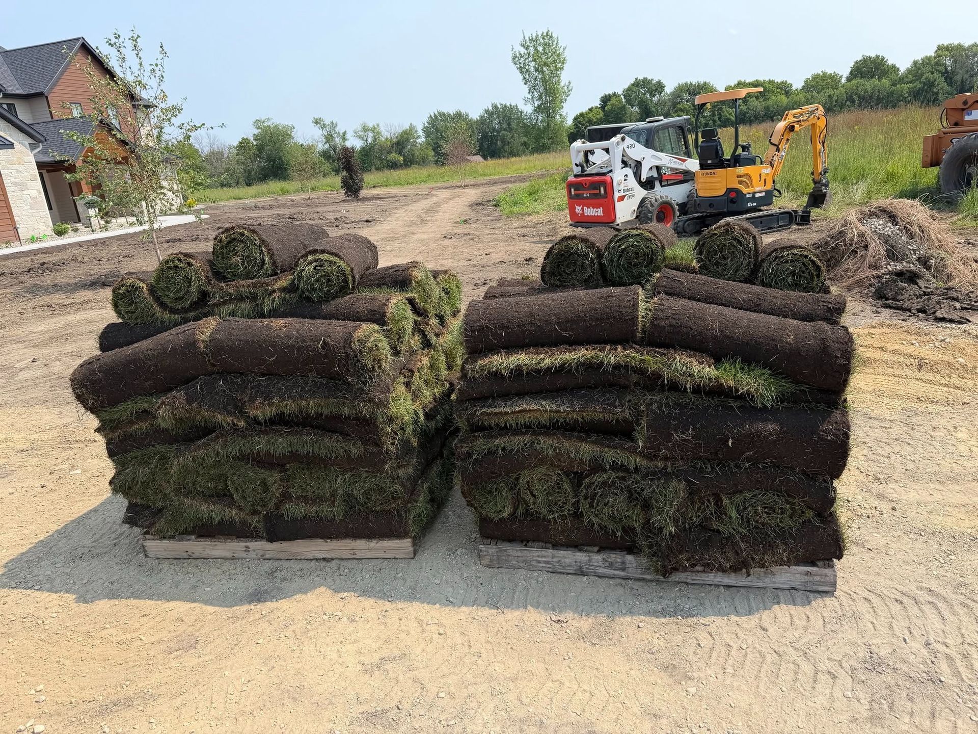 Stacks of rolled sod on a dirt field with workers and machinery in the background
