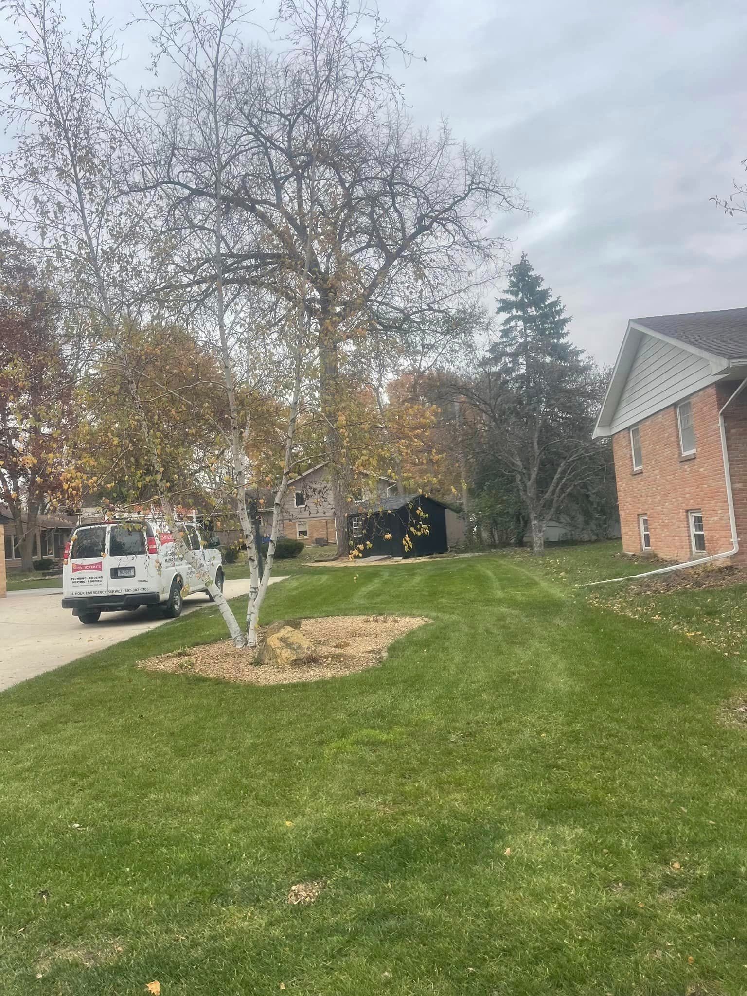 Suburban street with a parked white truck, leafless tree, grassy hill, and brick house under cloudy skies