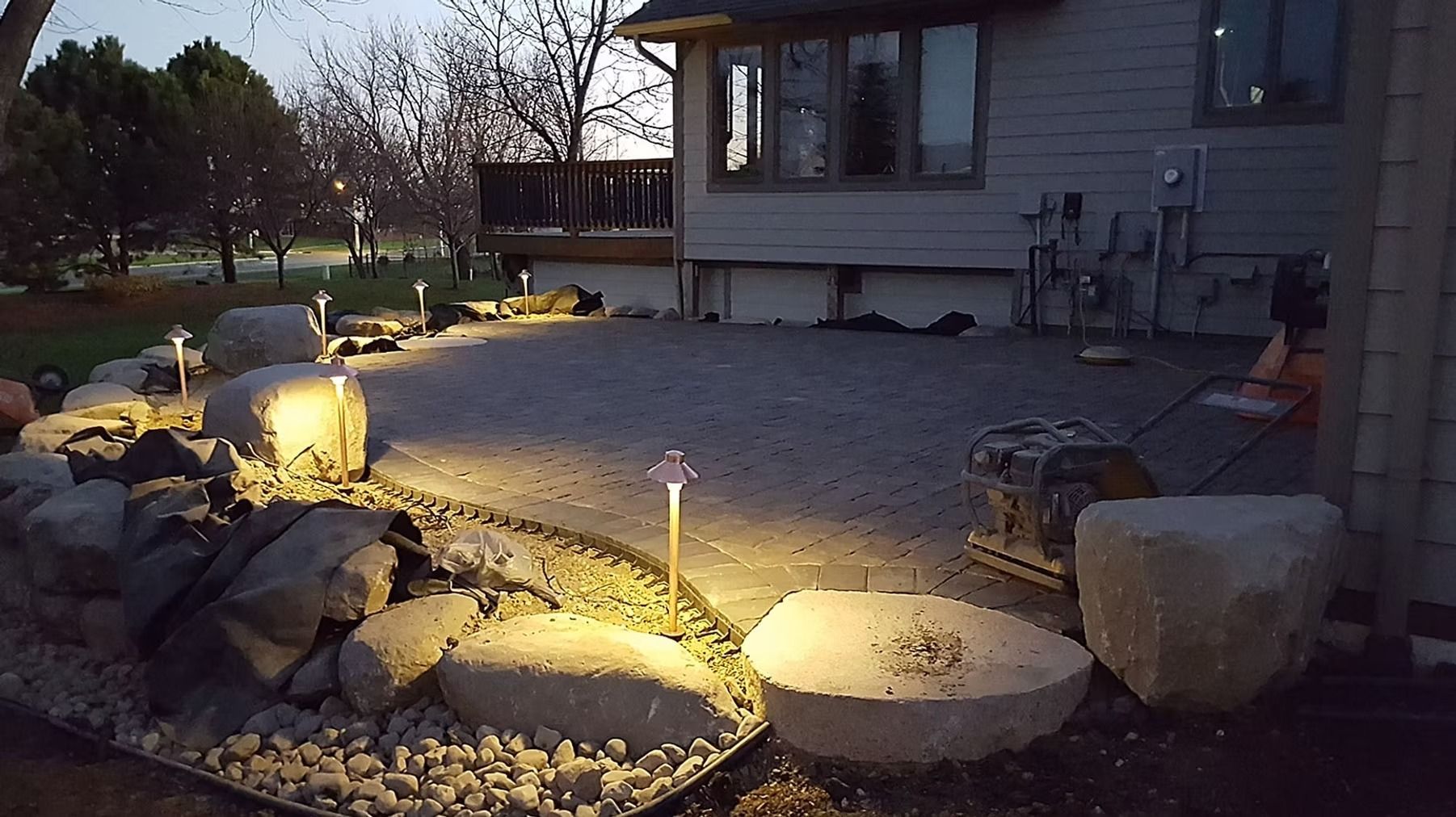 Lit backyard garden with rocks, gravel, and a house exterior at dusk