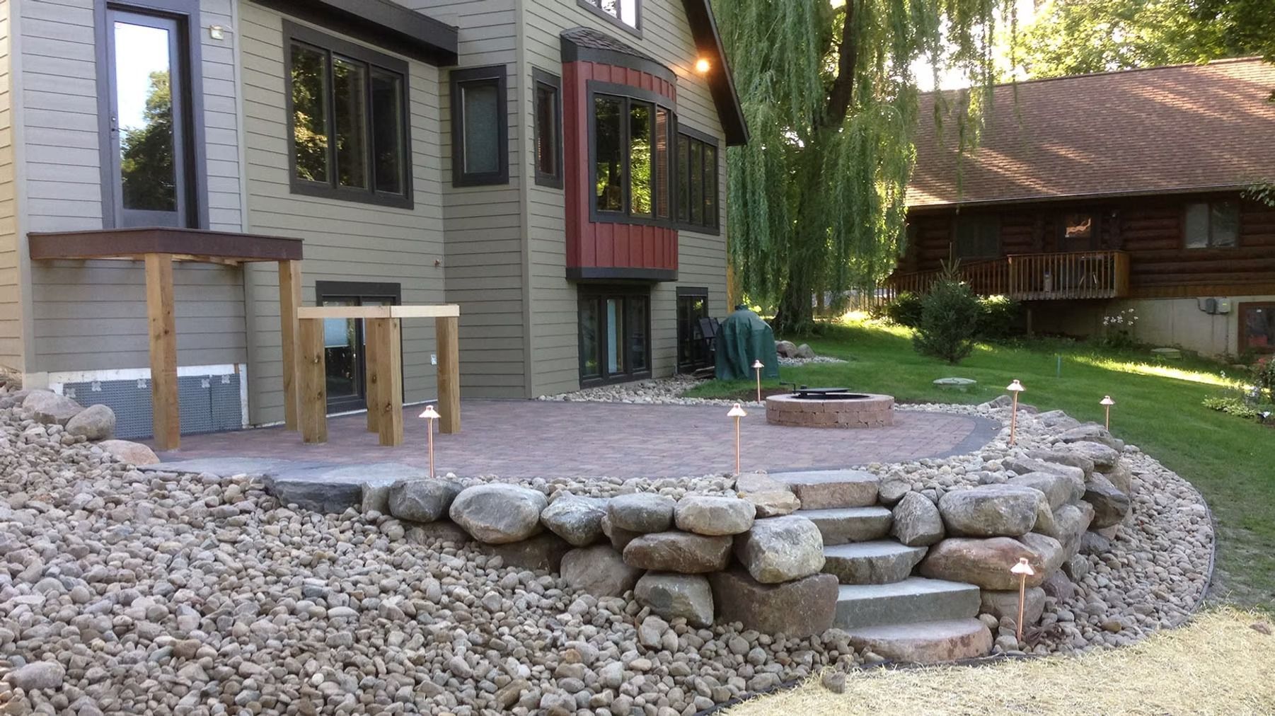 Backyard patio with stone retaining wall, gravel path, and house exterior with red-trimmed window