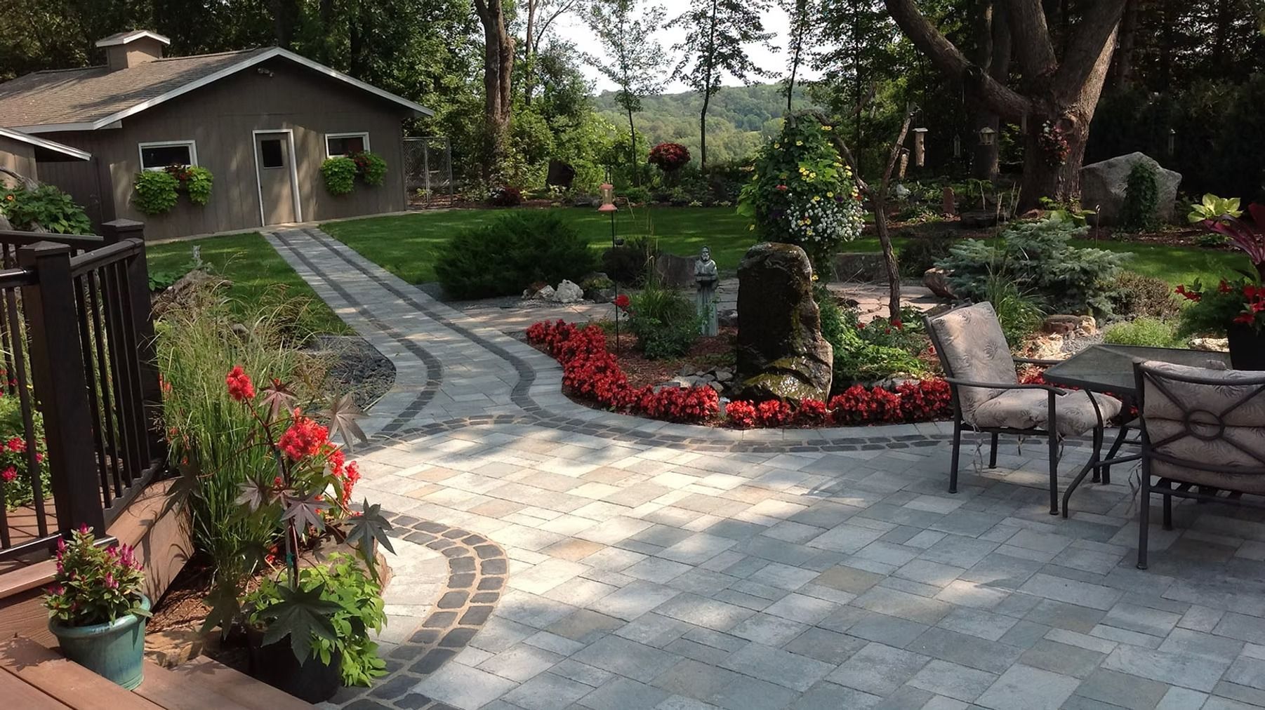 Patio garden with stone walkway, red flowers, and outdoor chairs beside a house