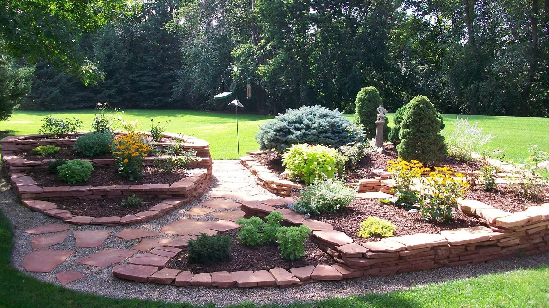 Curved stone flower bed with colorful plants and mulch in a sunny garden lawn