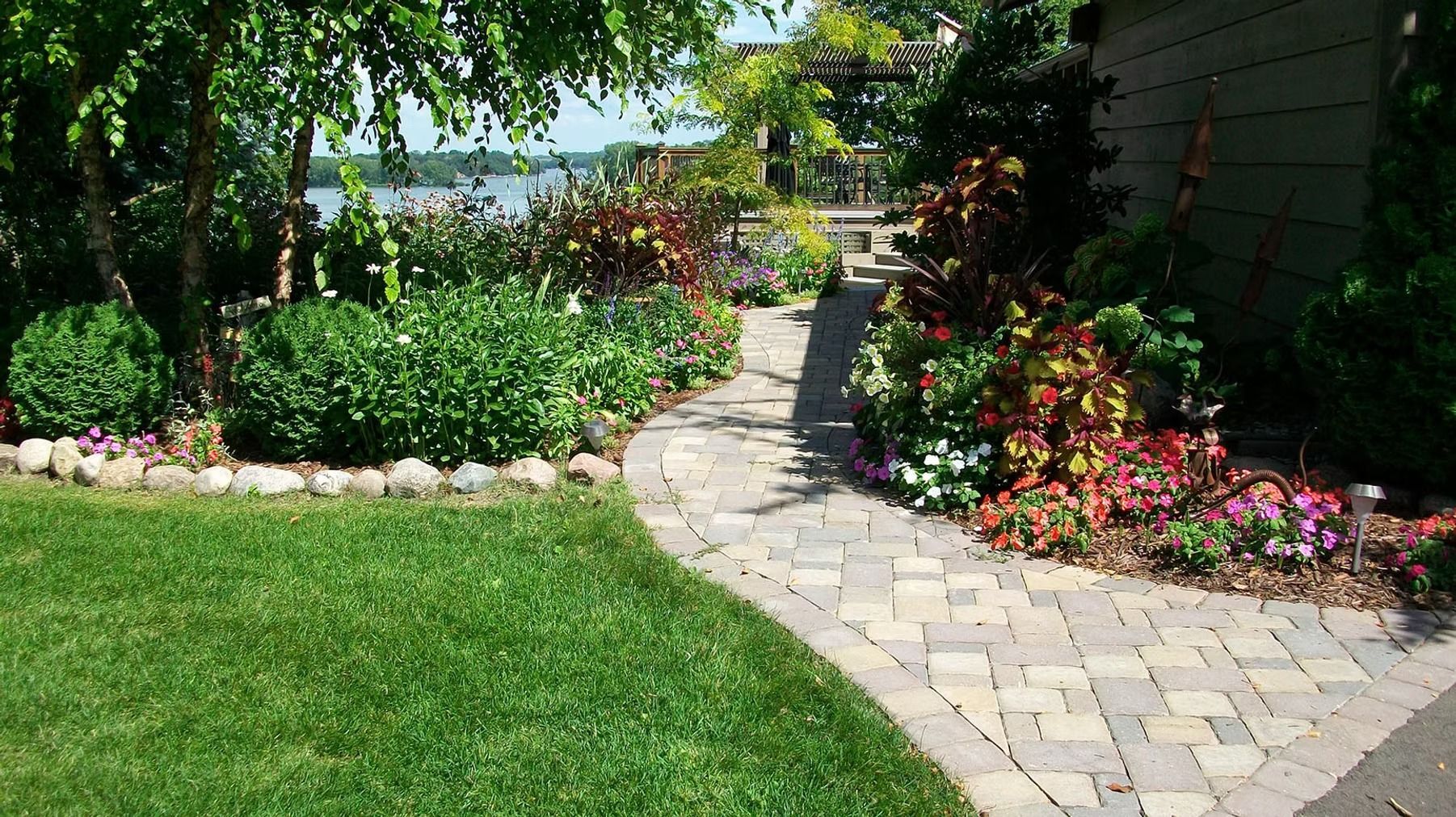 Curved stone garden path beside lush green lawn and colorful flower beds in a sunny yard