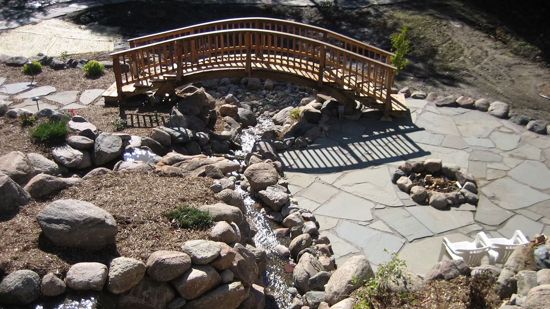 Small wooden footbridge over a rocky garden stream beside a stone path