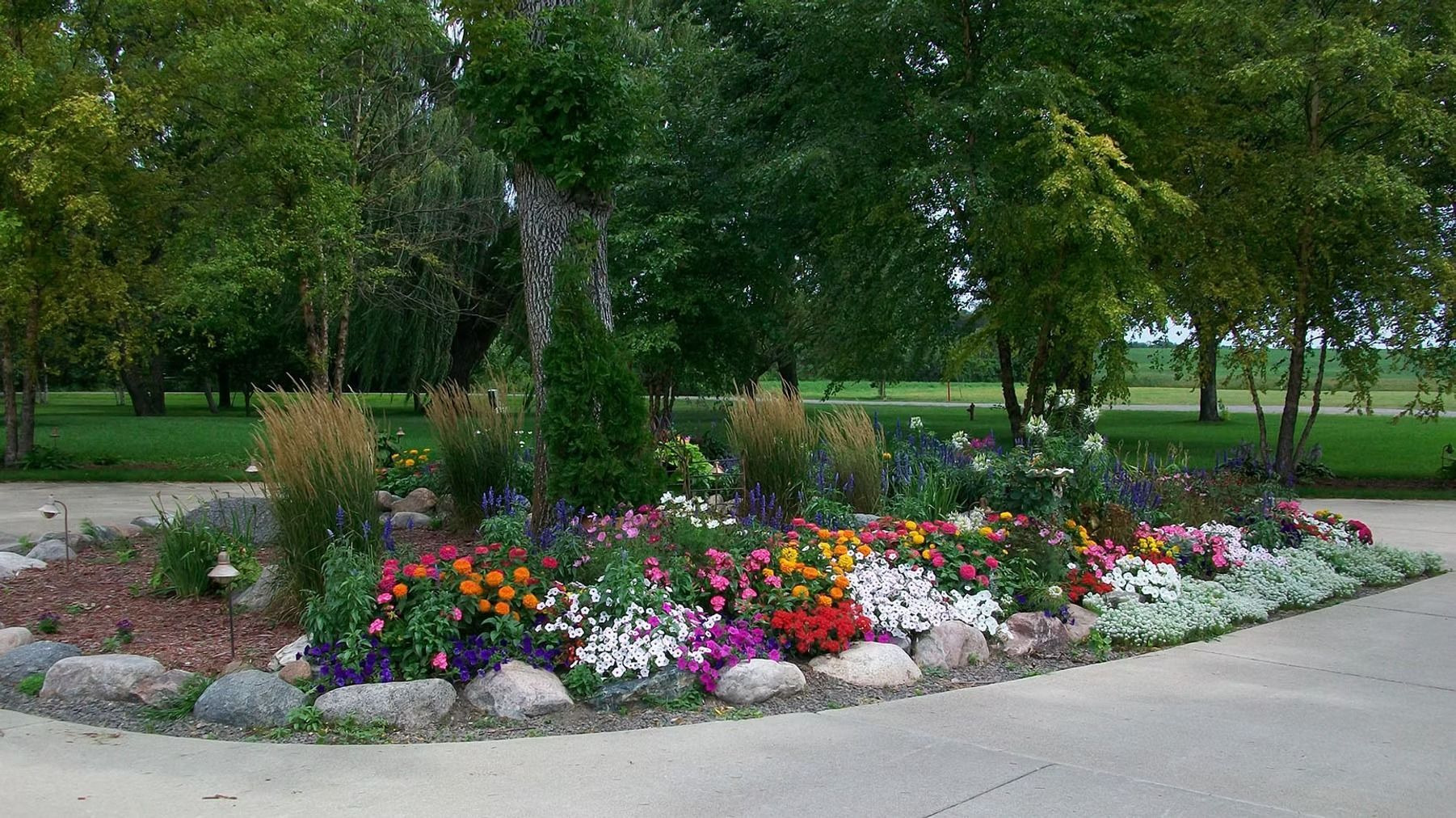 Colorful flower bed with rocks along a paved path in a green park