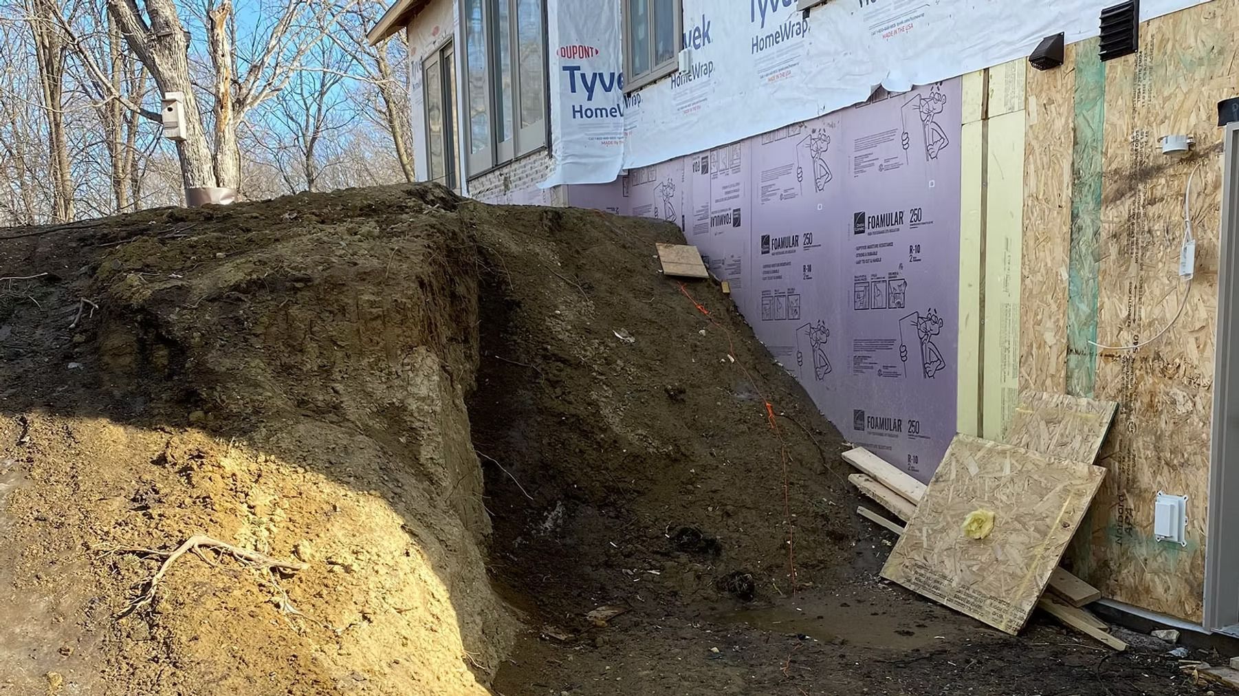 Large dirt mound beside a partially built house with exposed framing and construction wrap