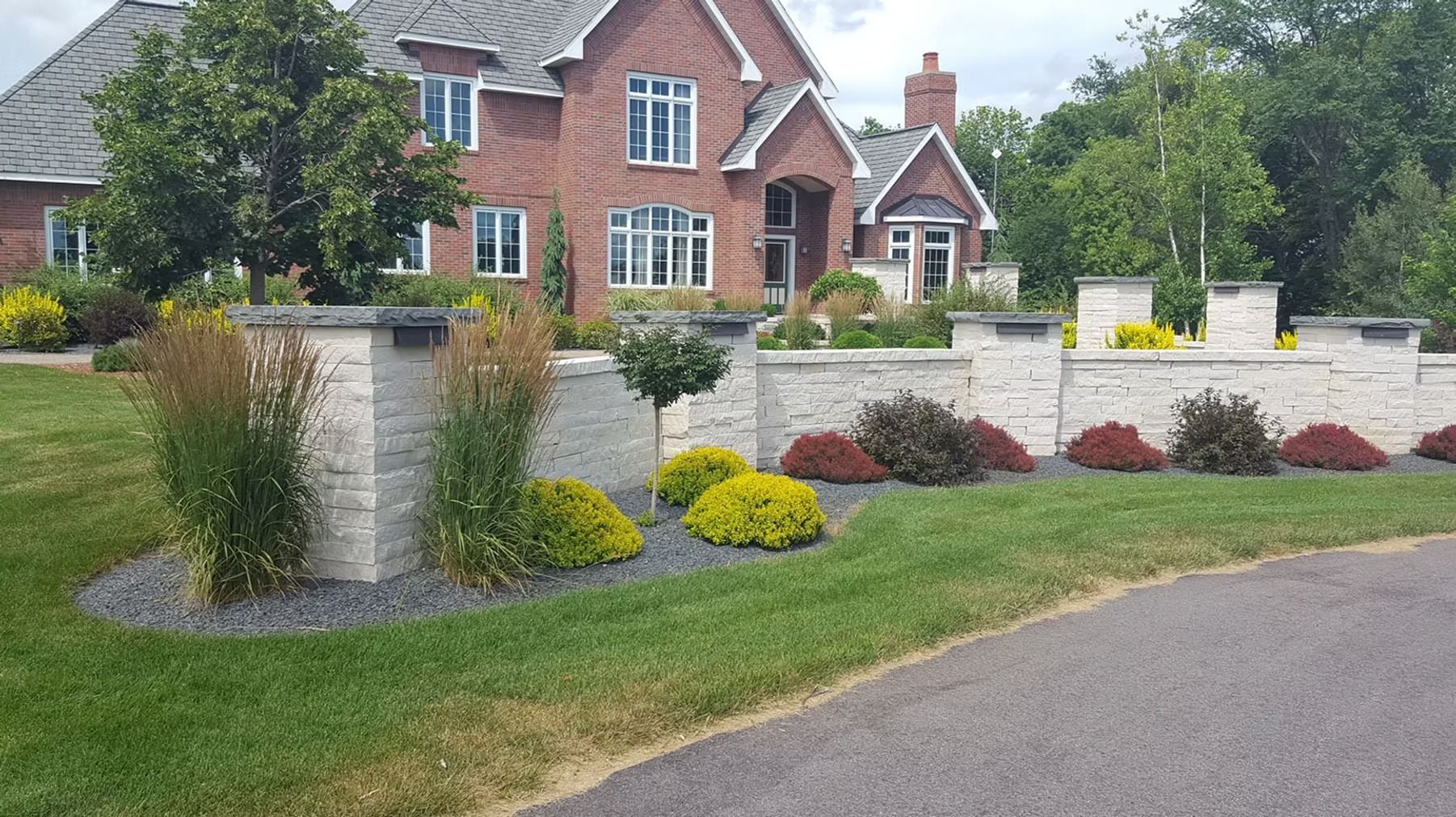 Large brick house with a manicured front garden, stone wall, and curved driveway.