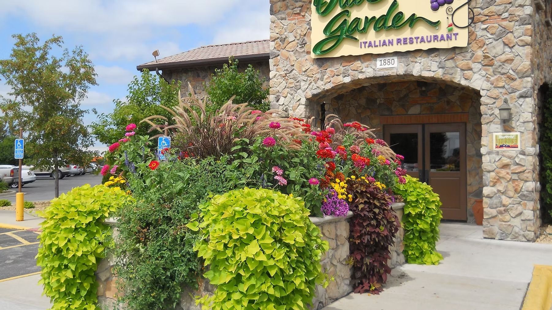 Stone restaurant entrance with colorful flower planters and green shrubs by the sidewalk
