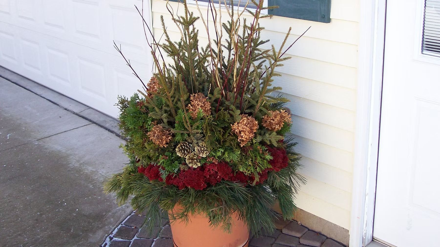 Potted autumn floral arrangement with red and green foliage beside a garage door
