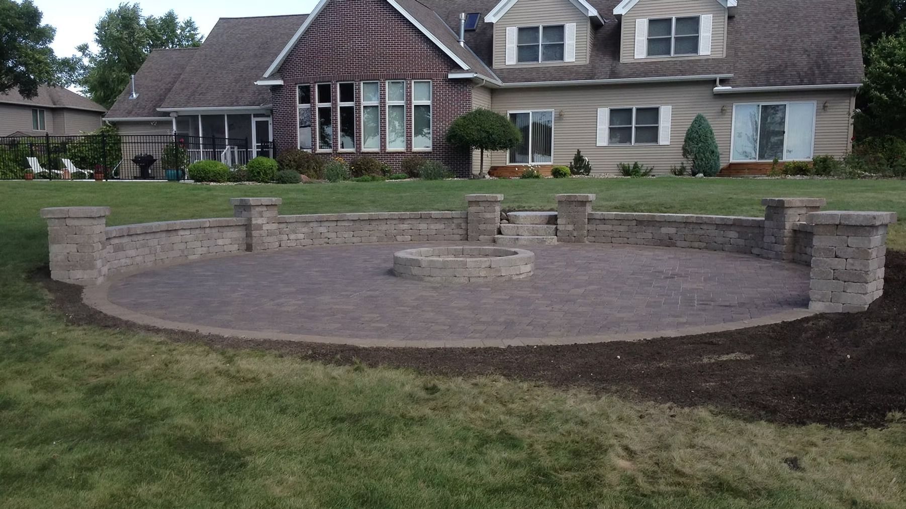 Circular brick patio under construction in a backyard, with a house in the background.