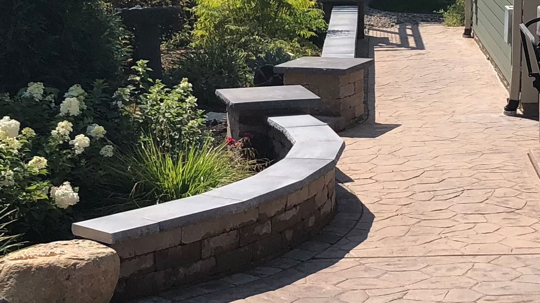 Curved stone bench beside a brick walkway in a sunny garden