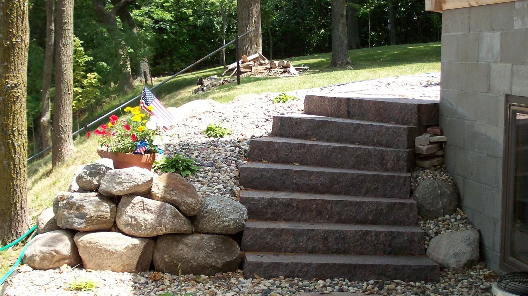 Stone steps beside a stacked rock wall leading up a wooded hillside with a small colorful flag