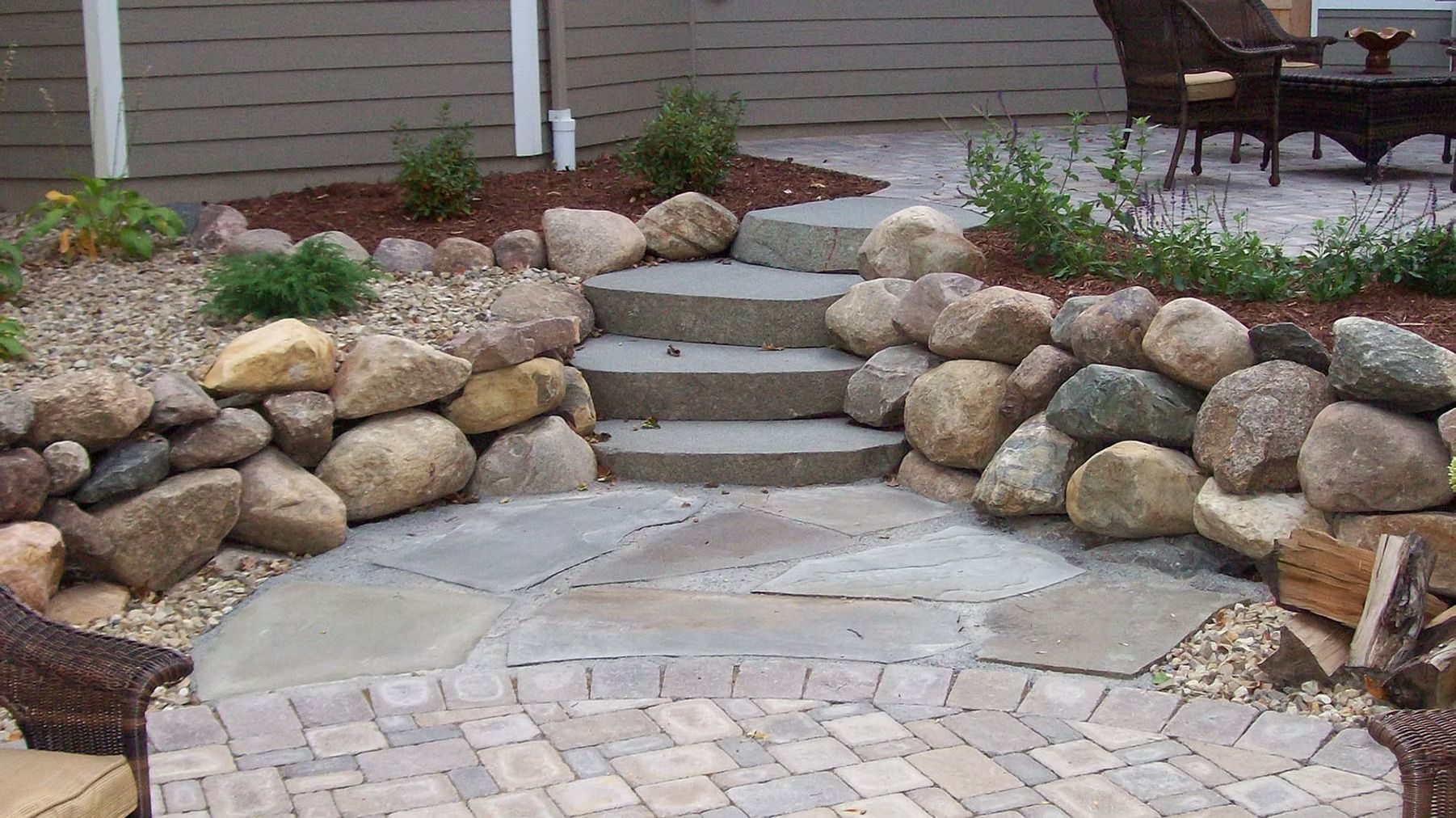Stone steps and landscaped rock garden leading to a house entrance with a brick patio