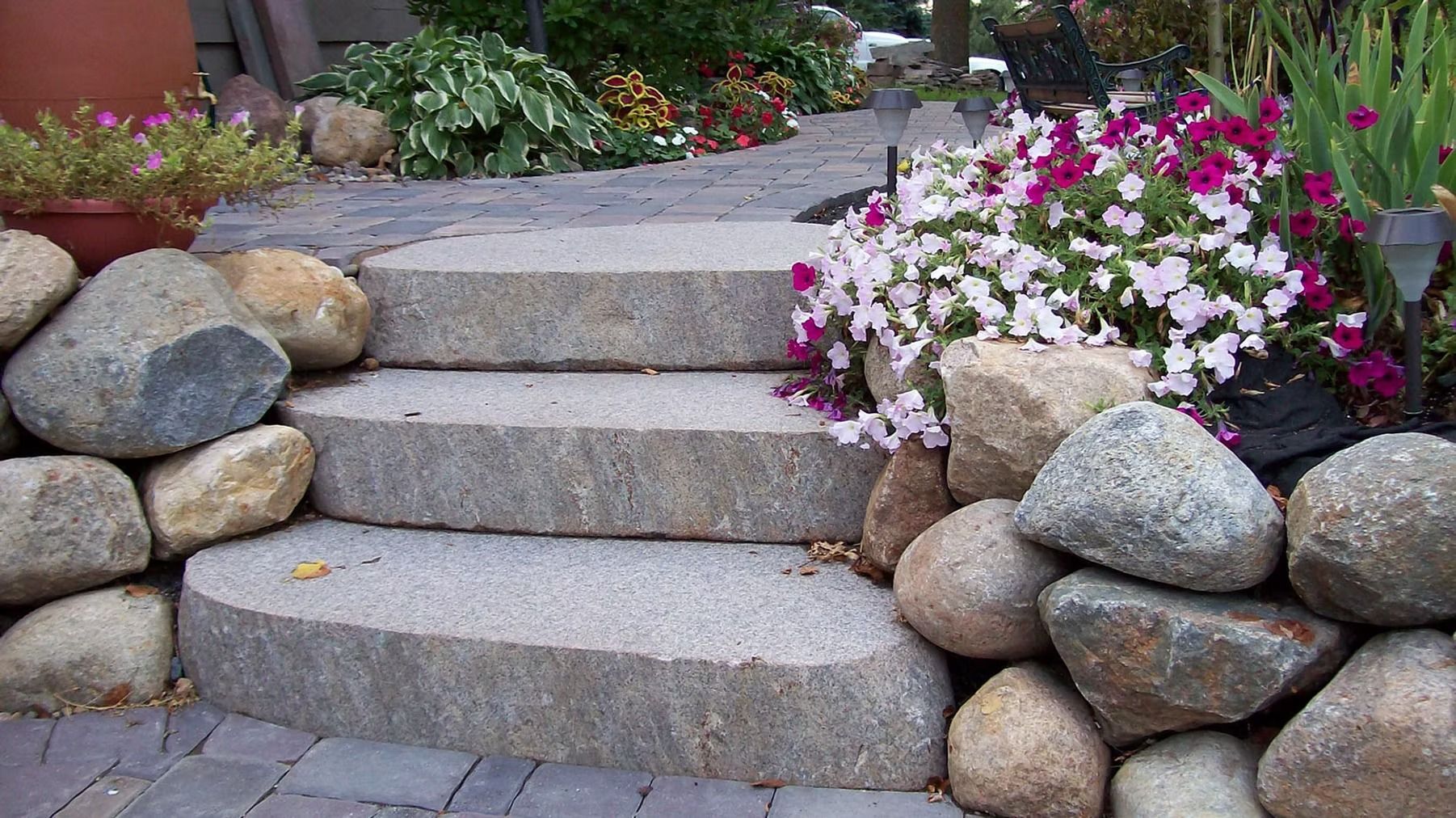 Stone garden steps bordered by rocks and pink-white flowers in a landscaped yard