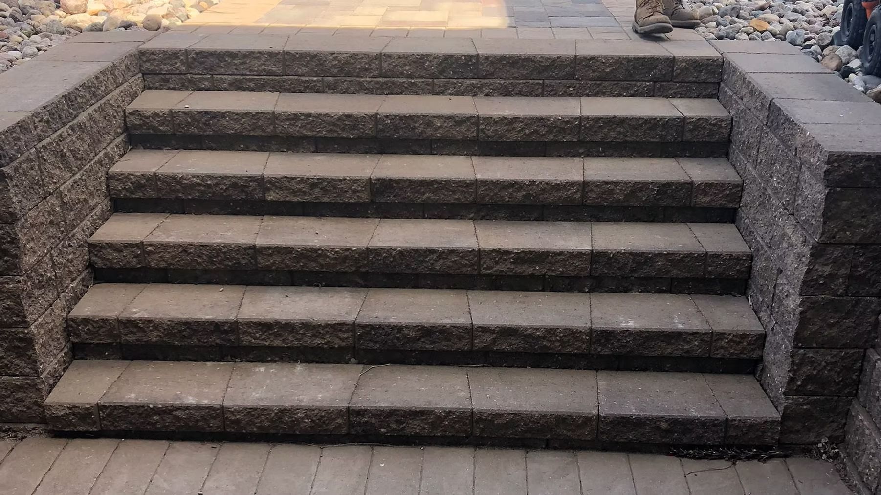 Stone steps with dark side walls leading up to a paved walkway outdoors