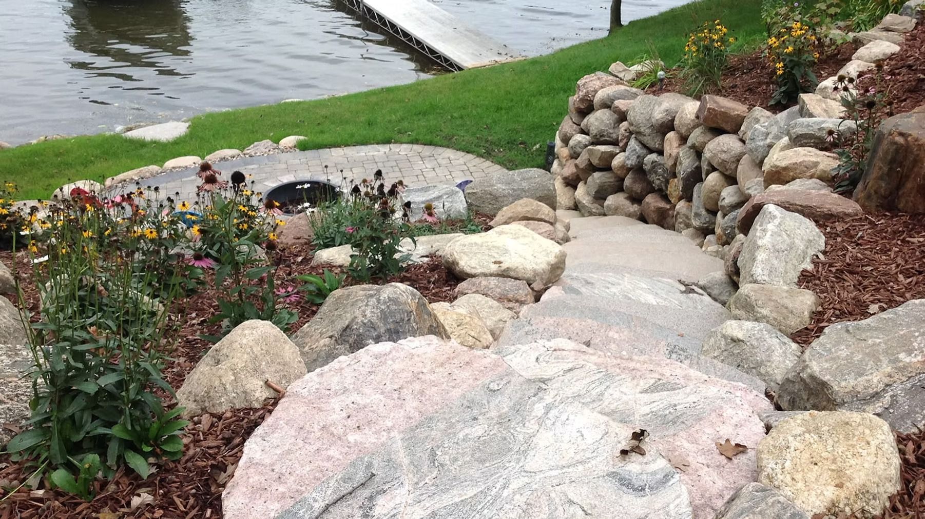 Rock garden path with large stones and flowers beside a pond and waterfall wall