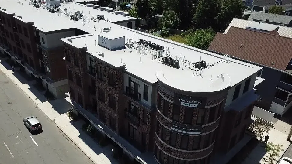 Aerial view of a multi-story brick apartment building with a rounded corner. Cars drive on the street below.