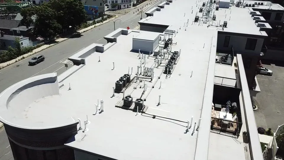 Aerial view of a building roof with HVAC equipment, next to a street with cars and trees.