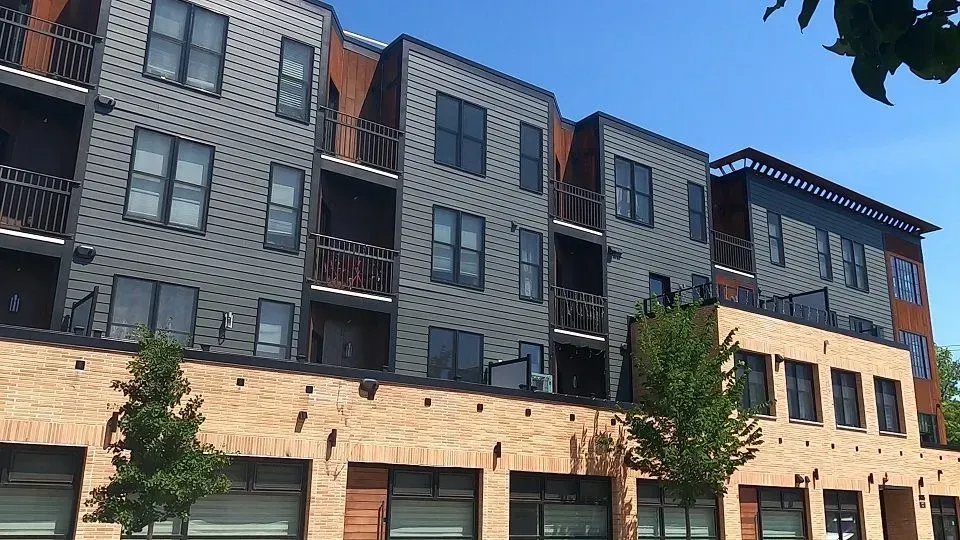 Multi-story building with gray siding, brick facade, and balconies.
