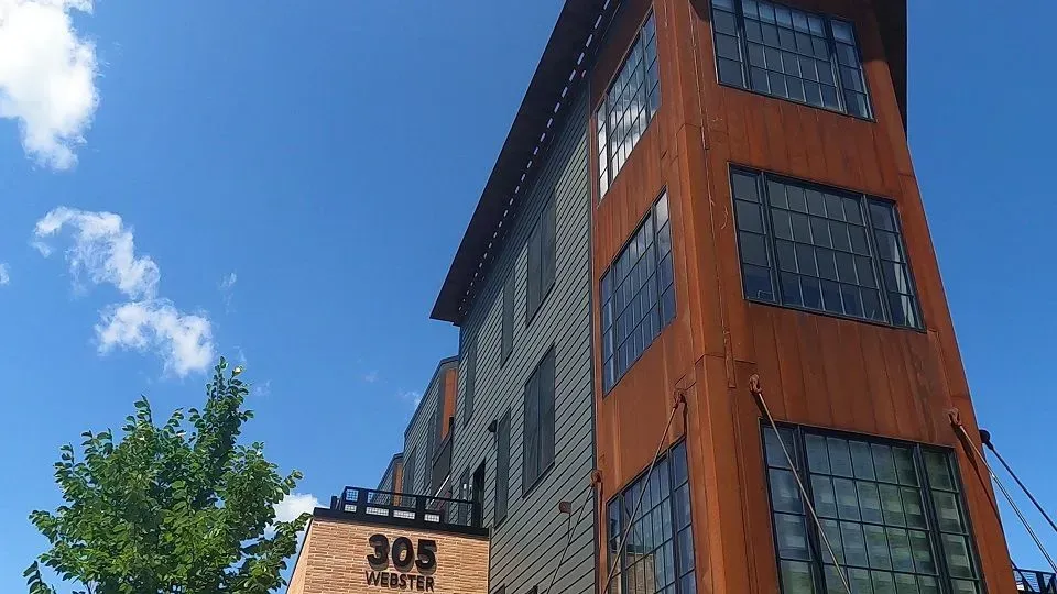 Modern building with rust-colored metal and gray siding against a blue sky, with the address 