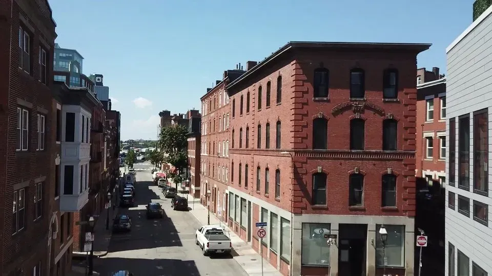 Street scene in Boston with brick buildings and cars driving down the road under a blue sky.