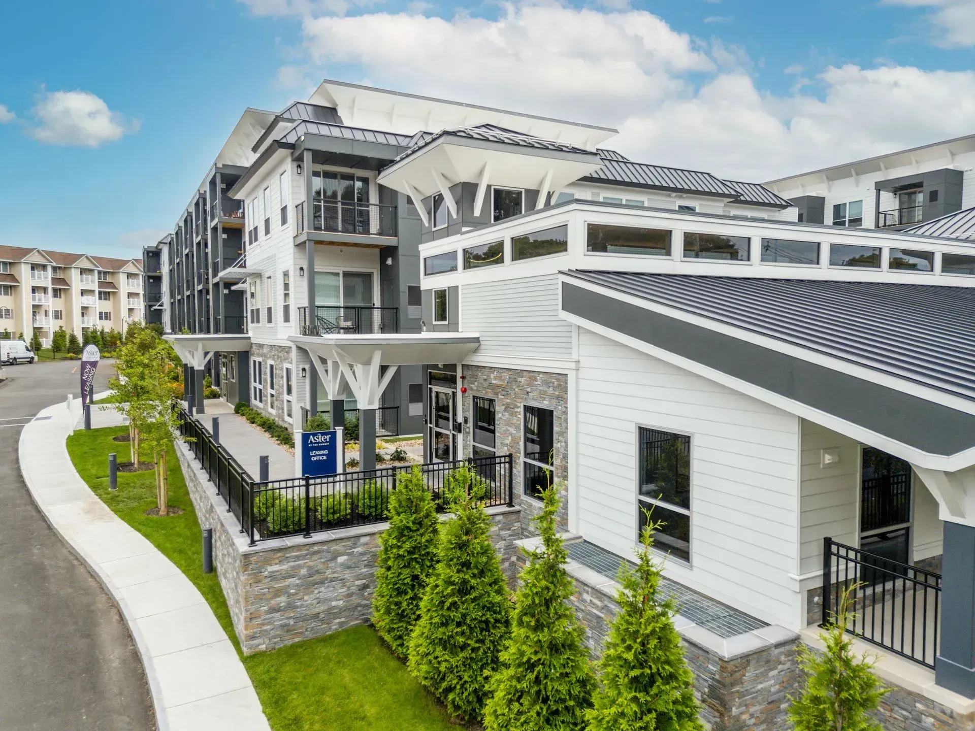 Modern apartment building with white and gray exterior, landscaping, and blue signage.