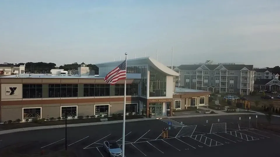 YMCA building with an American flag; parking lot in front; apartment buildings in background.