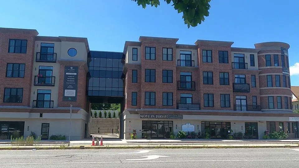 Multi-story brick building with storefronts and balconies, connected by a glass structure, under a blue sky.
