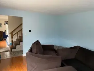 Living room with dark brown sectional sofa, light blue wall, and open view to staircase and hallway
