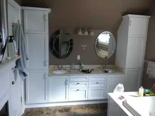 White bathroom vanity with two mirrors, sink, cabinet towers, and a bathtub in the foreground.