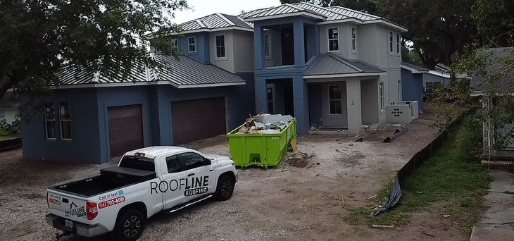 A white truck is parked in front of a large house under construction.