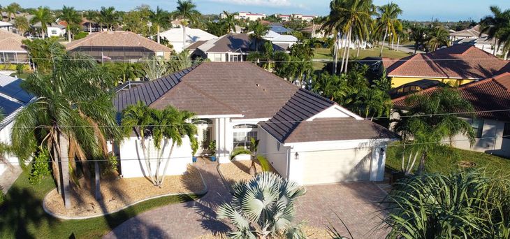 An aerial view of a house in a residential area surrounded by palm trees.