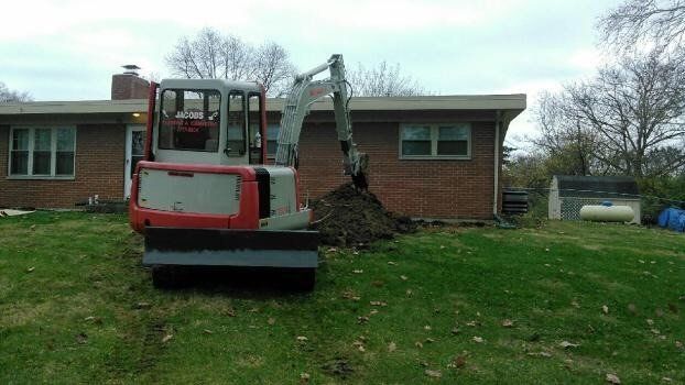 a small excavator is digging a hole in front of a brick house .