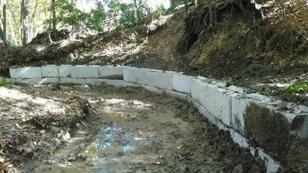 a concrete wall is being built in the middle of a muddy area in the woods .