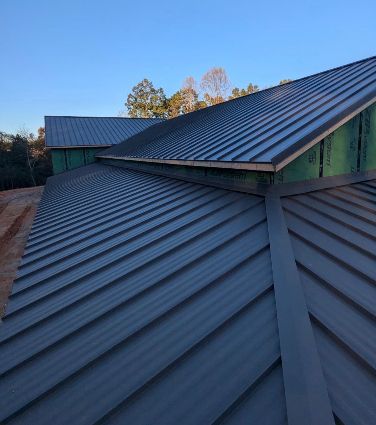 Blue metal roof with intersecting ridges on a house at dusk, with trees in the background