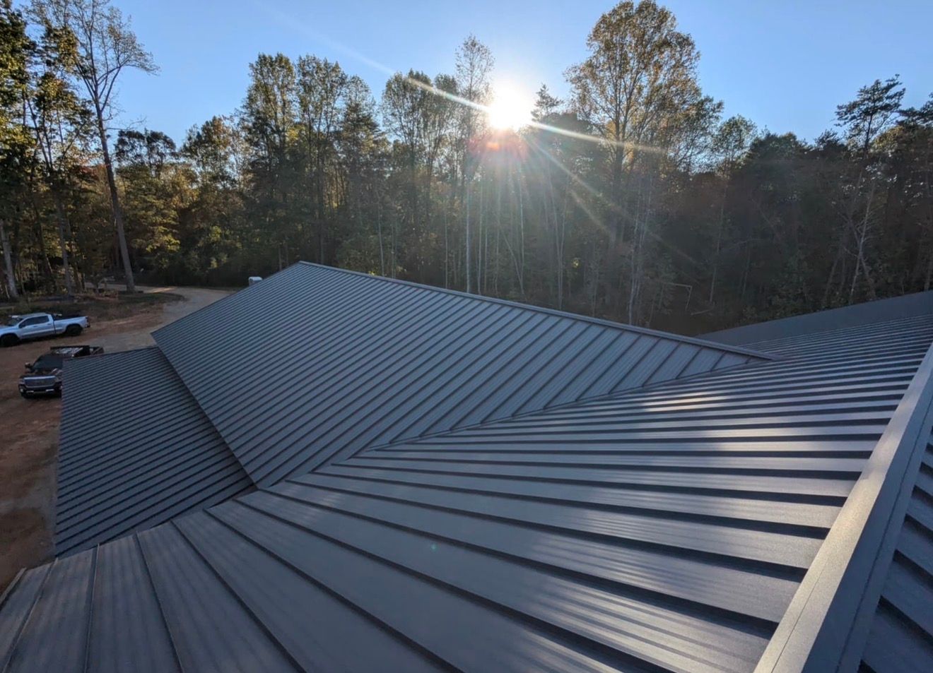 Dark gray metal roof with sun flare, viewed over wooded trees at sunse