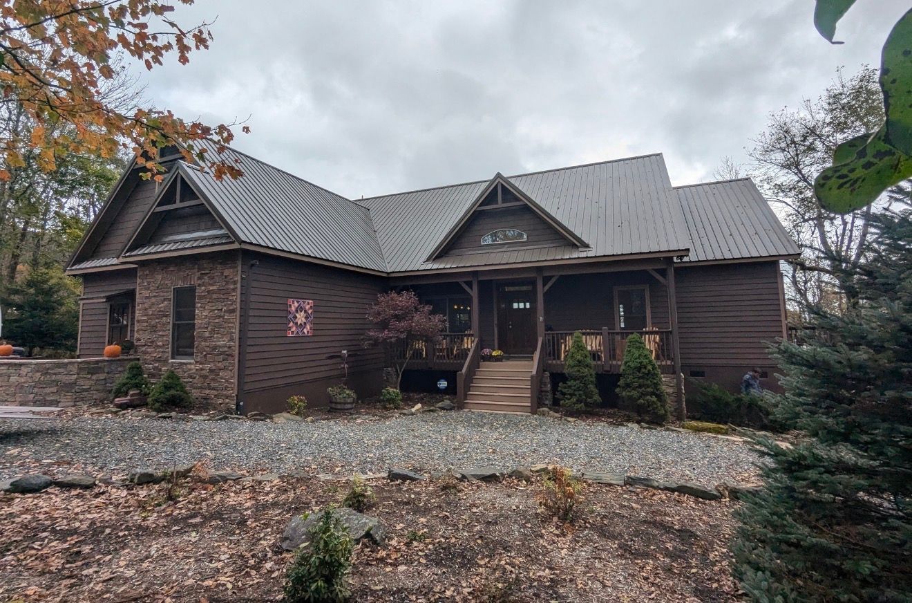 Rustic dark-brick cabin with a gray metal roof, front porch, and leaf-covered ground in autumn