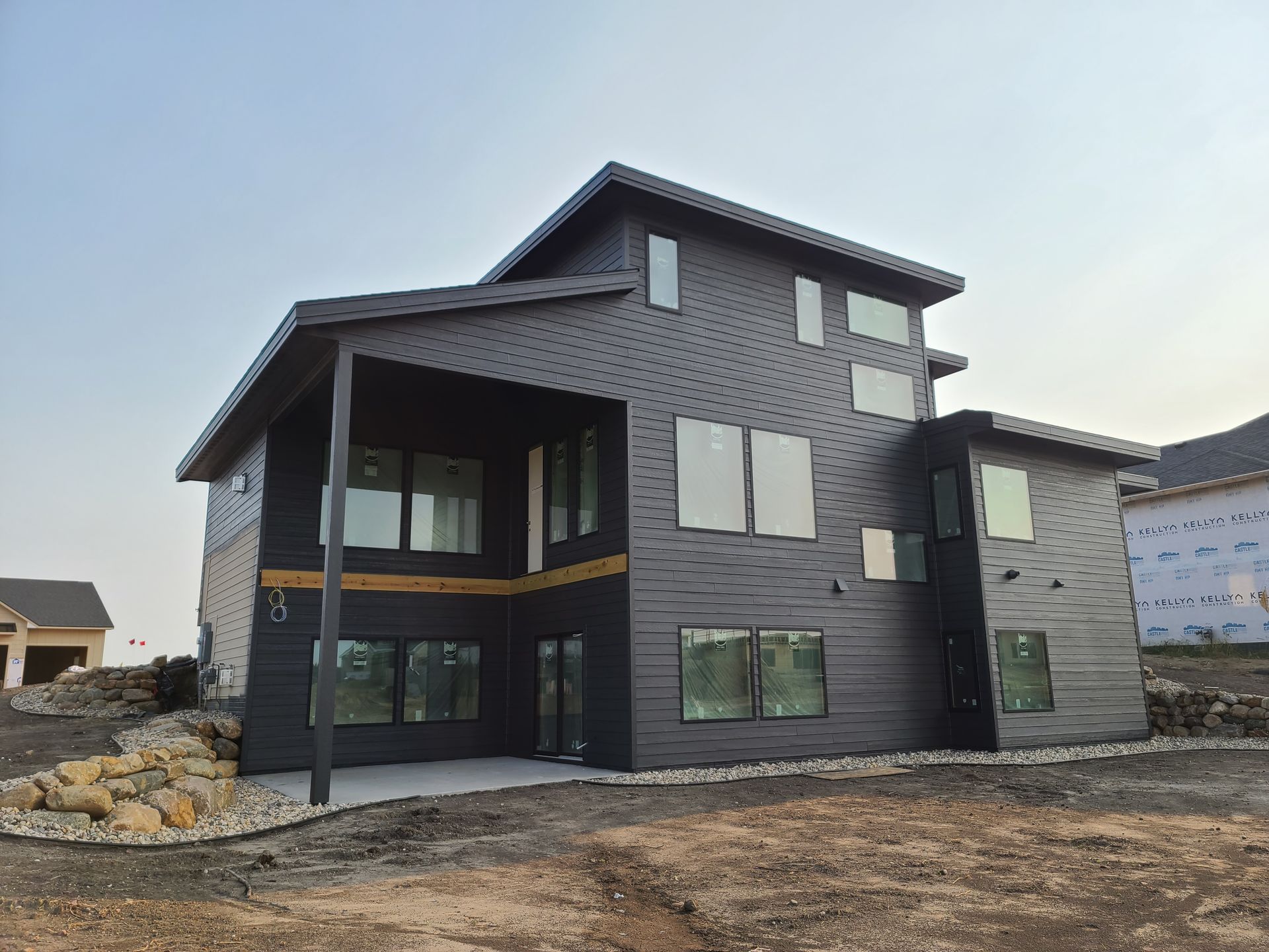 Modern two-story house with black siding, large windows, and a covered porch on a construction site.