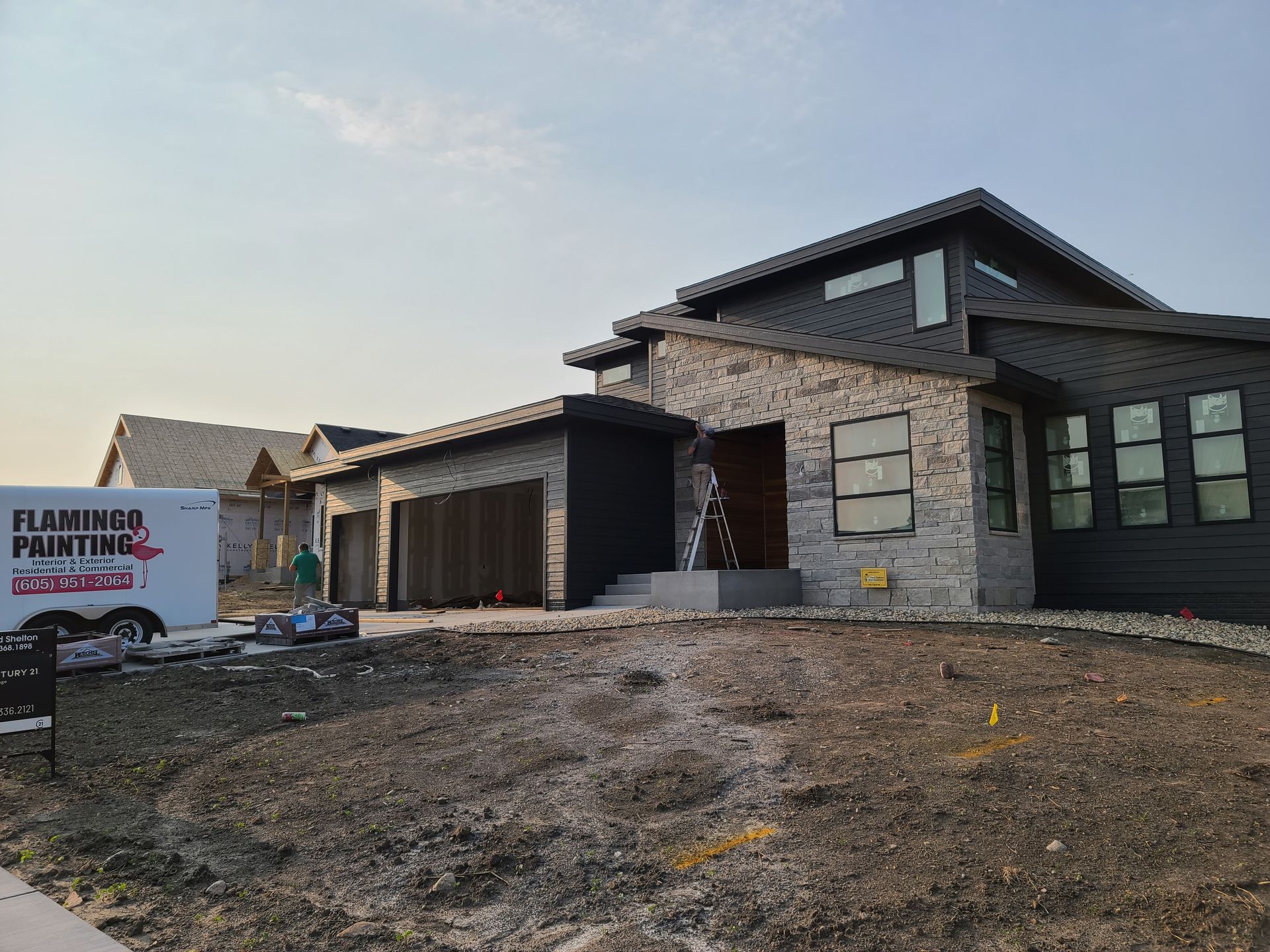 Modern home with stone facade and dark accents; Flamingo Painting van parked in front.