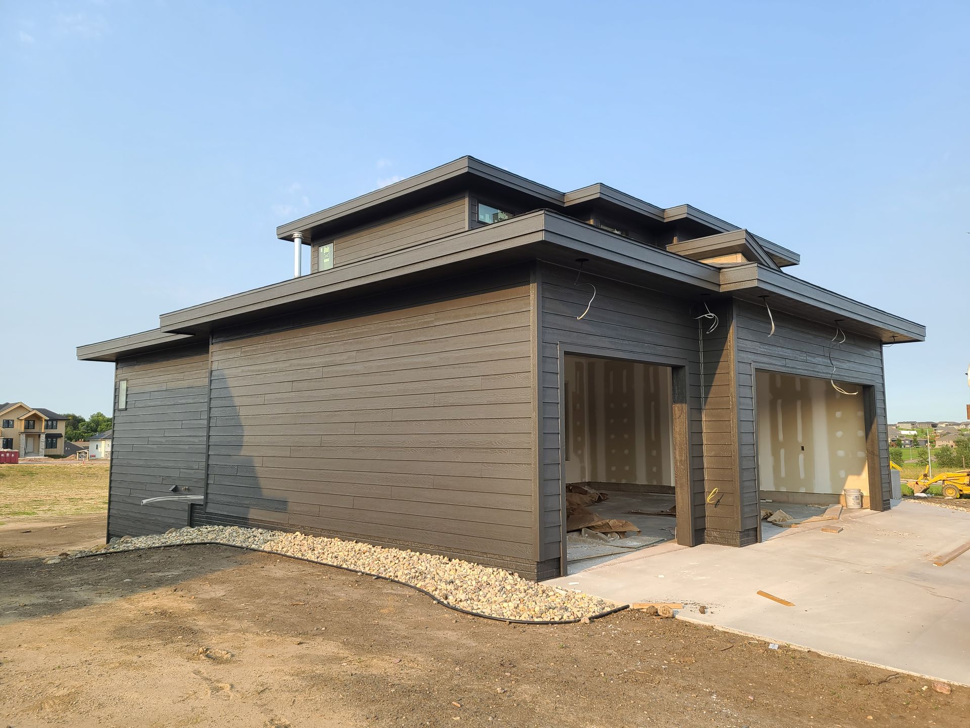 Dark grey modern building with two garage bays, under construction.