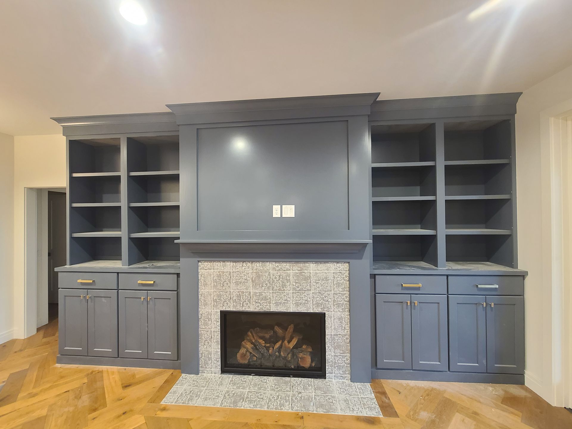 Built-in gray cabinetry with fireplace and bookshelves in a room with wood flooring.