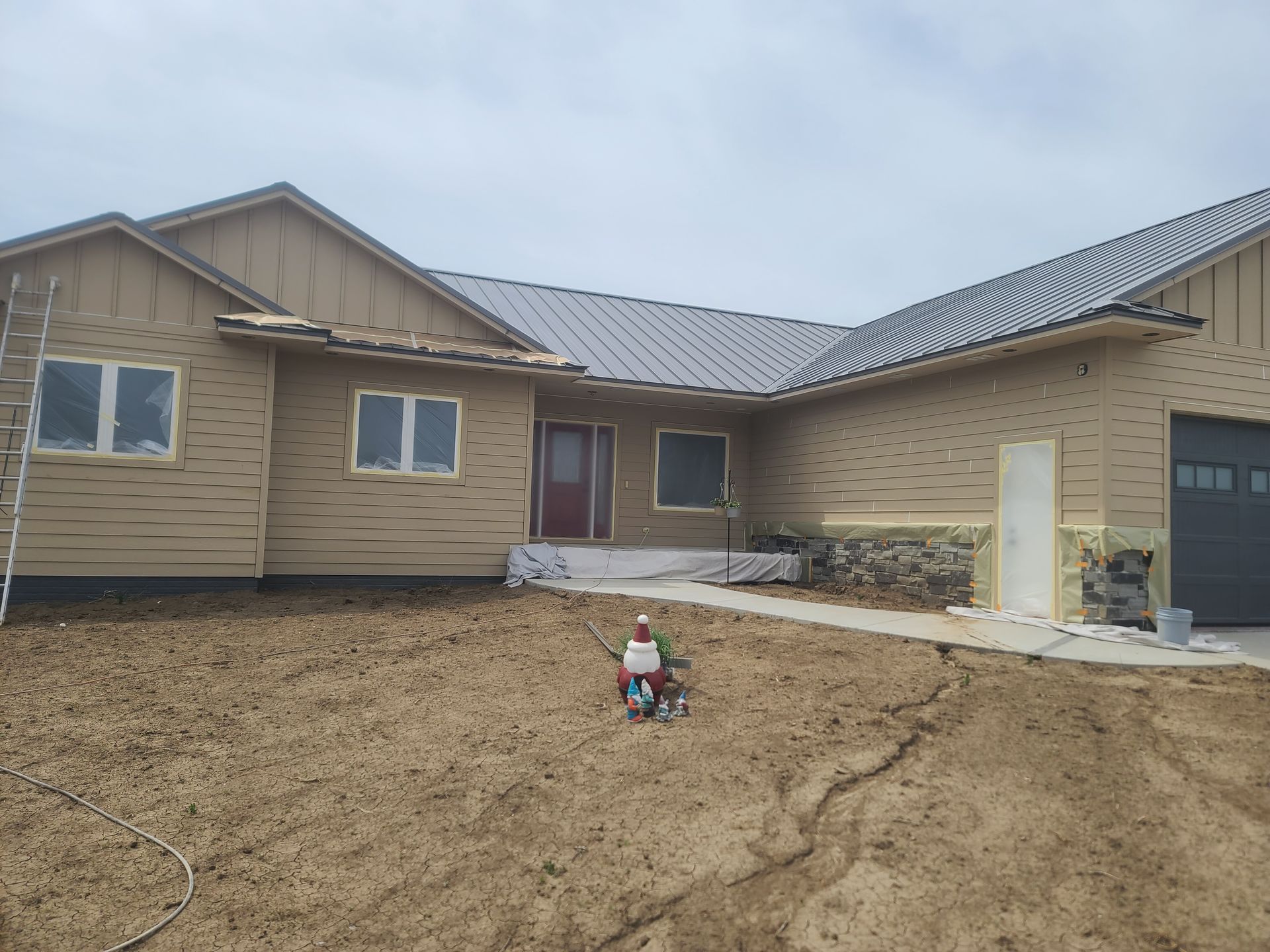 Tan house under construction; front yard with muddy ground, and a person spraying.