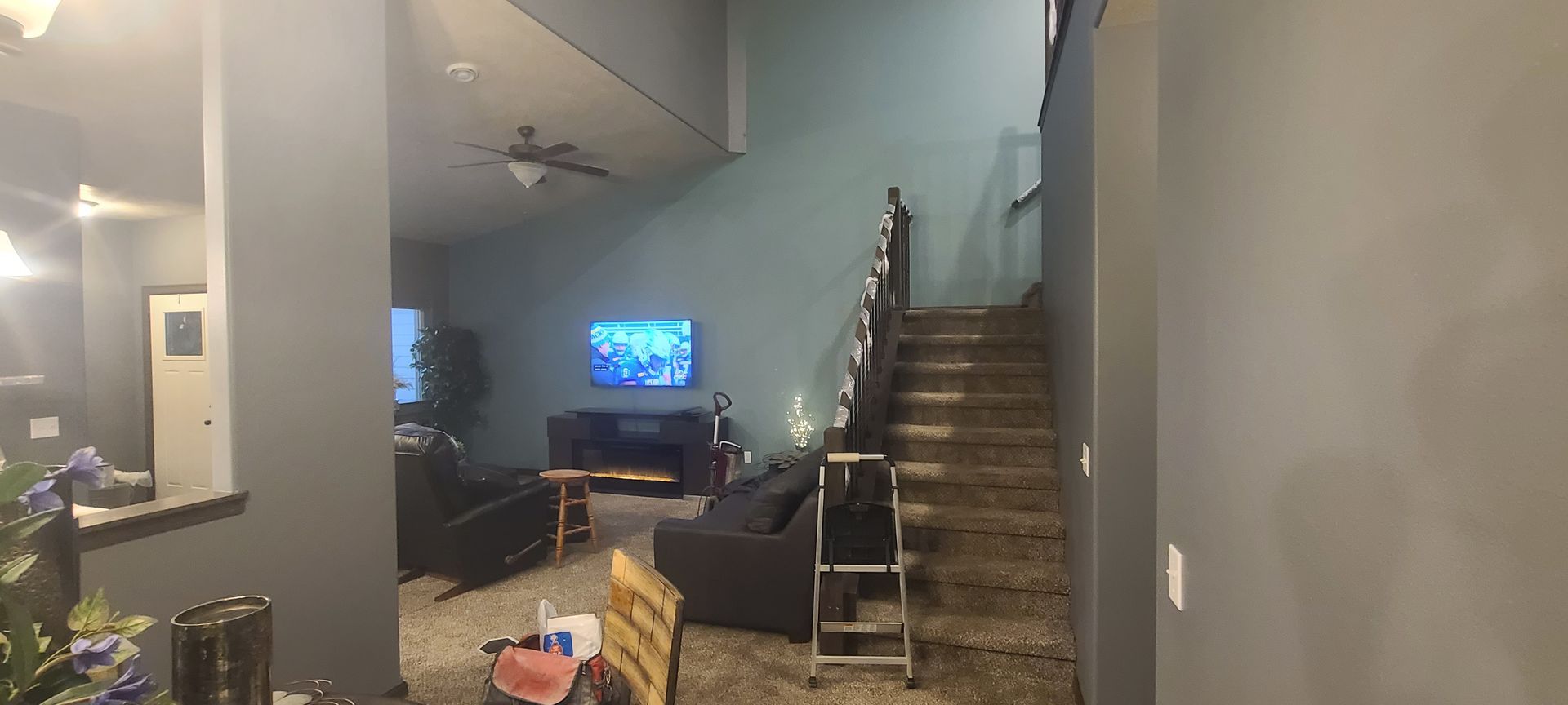 A living room with stairs. A TV is mounted, and a ladder sits in front of the stairs.