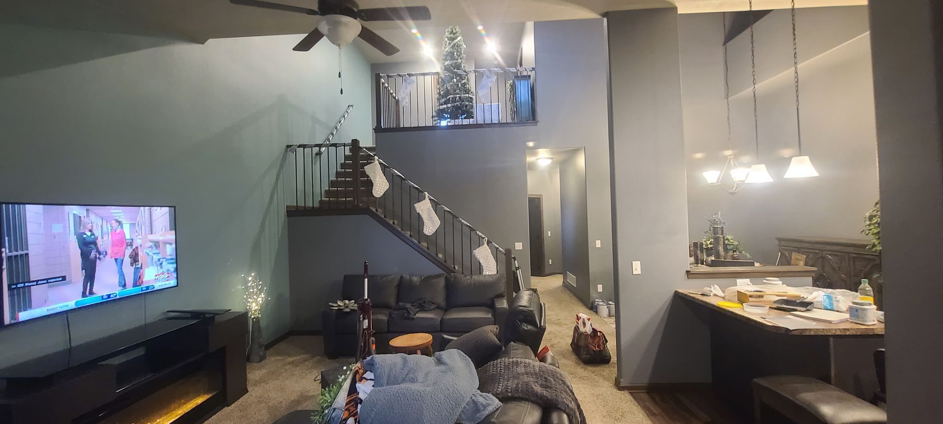 A modern living room with a staircase, Christmas tree on the mezzanine, and a TV playing a show.