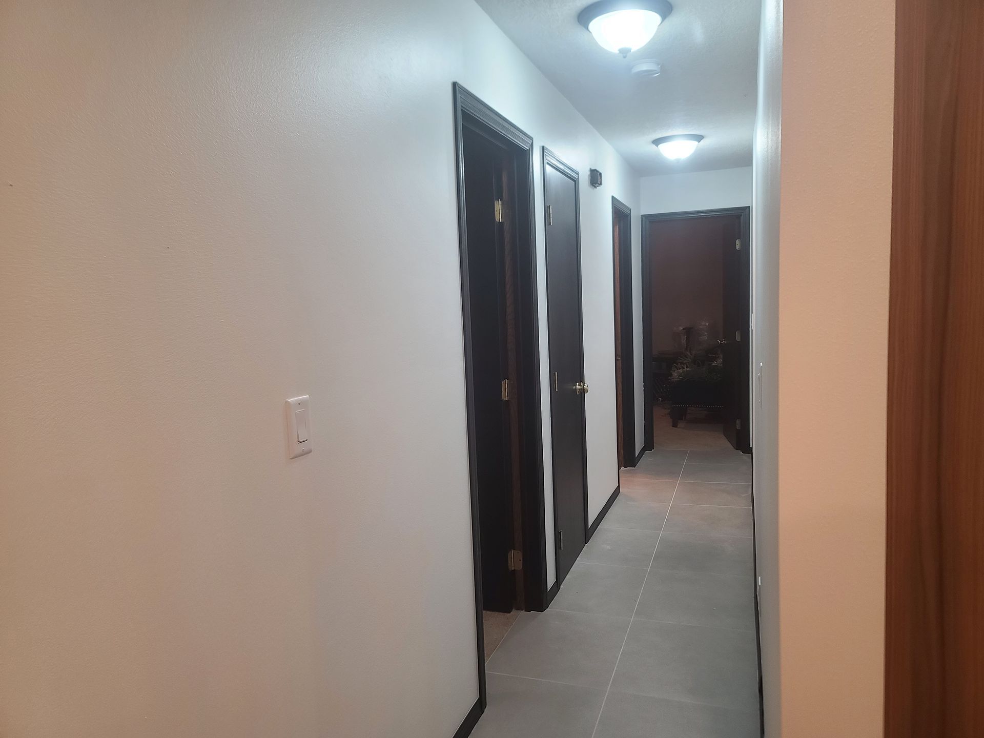 Long hallway with white walls, dark doors, and overhead lights.
