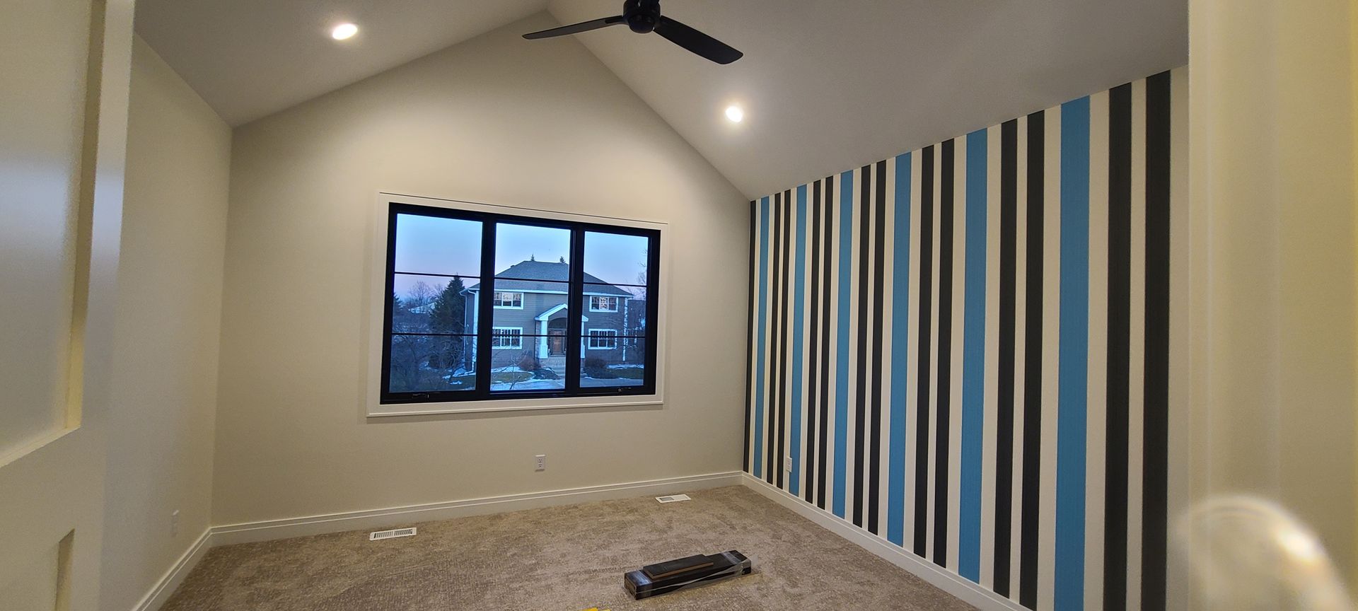Empty bedroom with a striped accent wall, window, and ceiling fan.